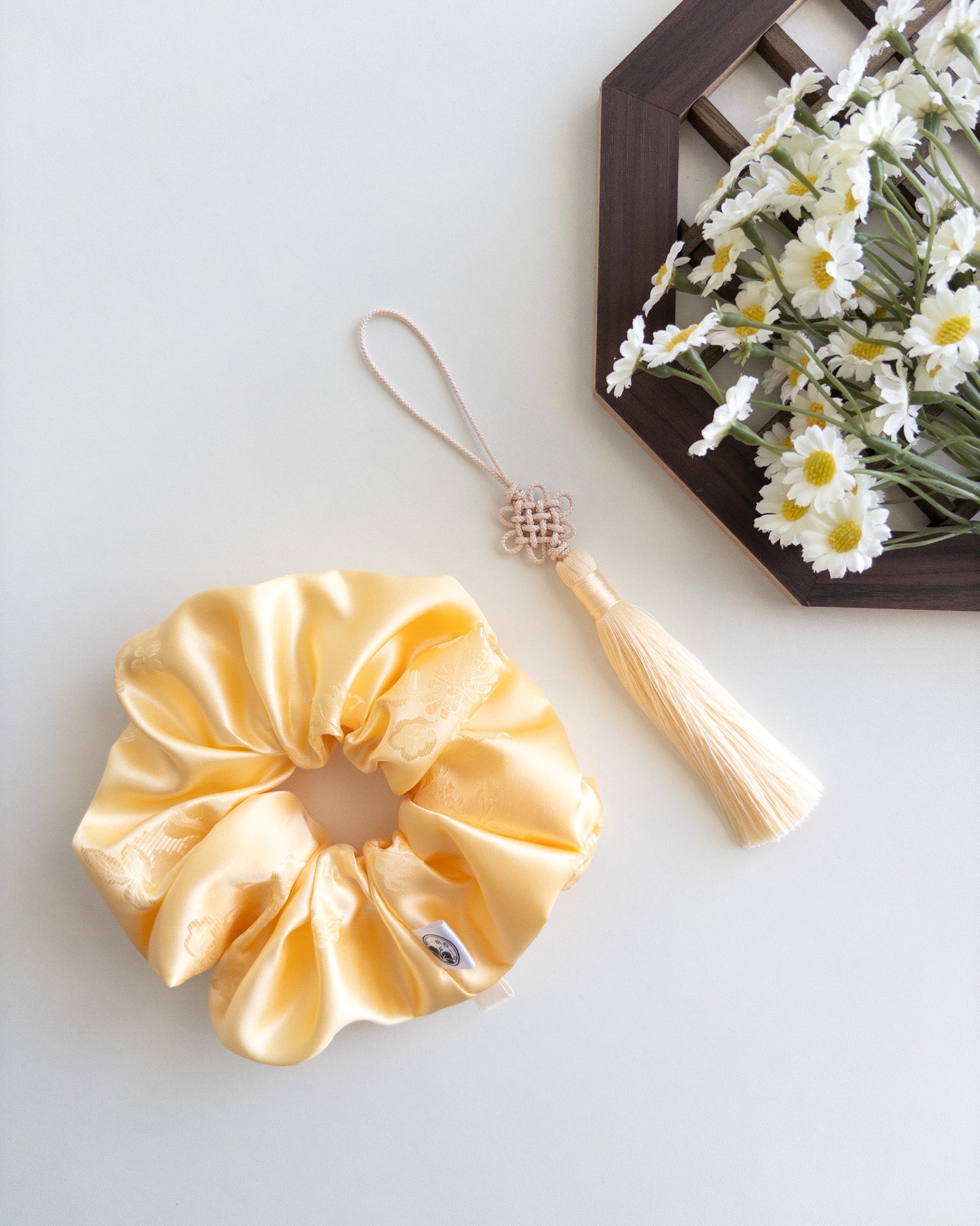 Yellow satin hanbok scrunchie with tassel on a light gray background