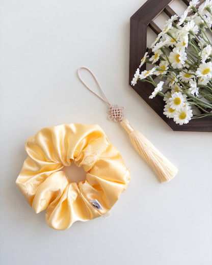Yellow satin hanbok scrunchie with tassel on a light gray background